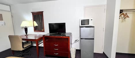 Une chambre d’hôtel équipée d’un lit, d’un bureau avec un ordinateur, d’une télévision, d’un four à micro-ondes et d’un réfrigérateur.