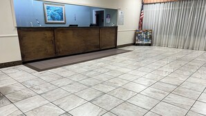 A reception area with a marble floor, wooden reception desk, framed artwork, and an American flag. - Heritage Inn and Suites (Baton Rouge)