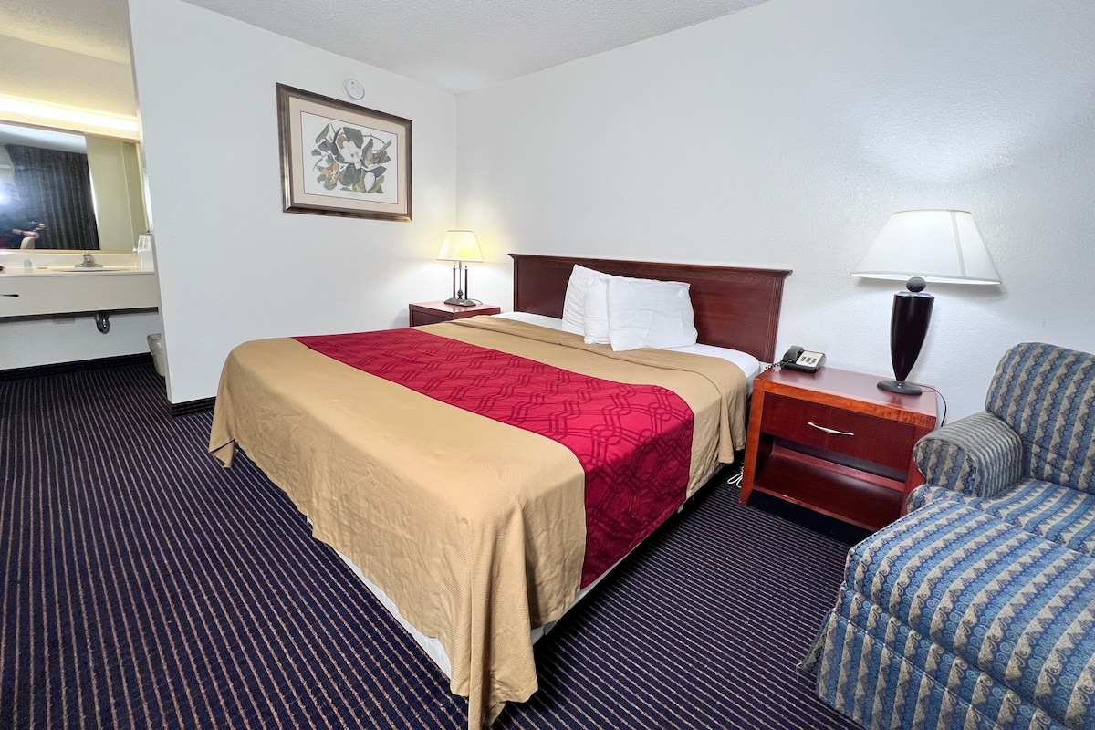 A hotel room with a bed, bedside tables, a chair, a mirror, and a framed picture on the wall.