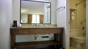 A bathroom with a wooden vanity, a mirror, a coffee maker, and a toilet visible through an open door.