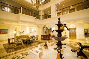 Un hall d’hôtel à plusieurs niveaux, doté d’une fontaine centrale, de coins salon et d’un lustre.