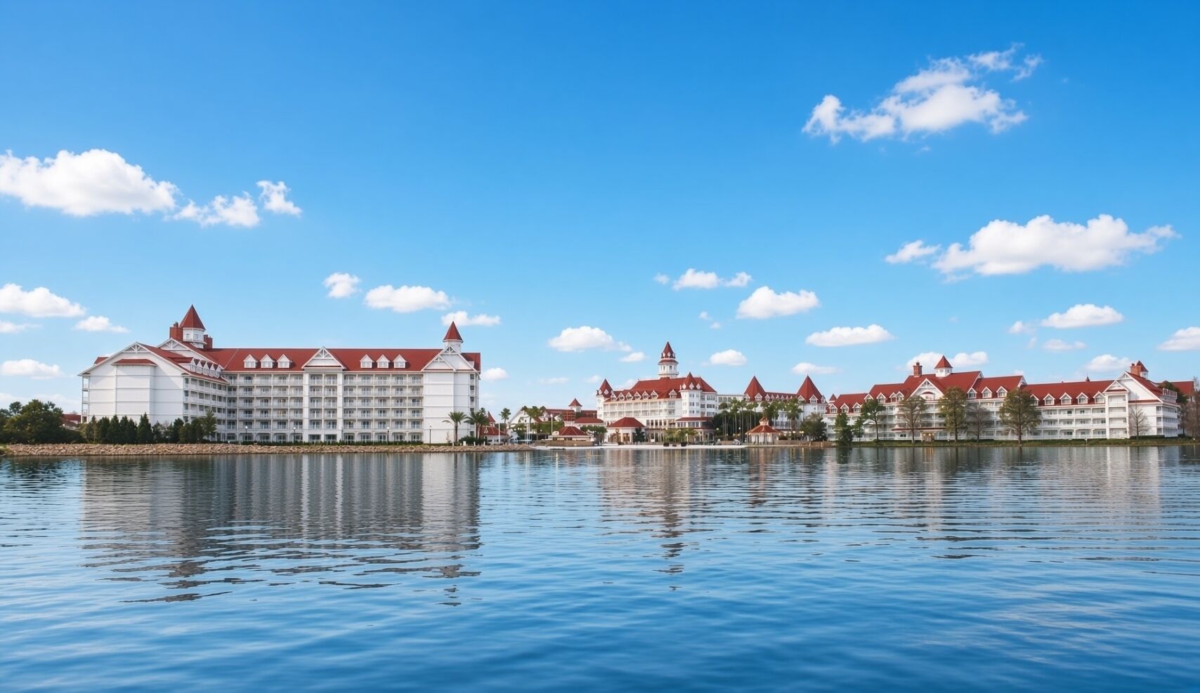 A large hotel with multiple buildings, a lake in the foreground, and a clear blue sky.