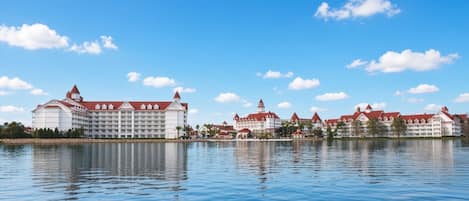 Un gran hotel con varias construcciones, un lago al frente y un cielo azul despejado.