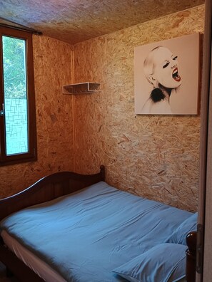 A room with a wooden wall, a bed with a headboard, a window, and a picture on the wall.