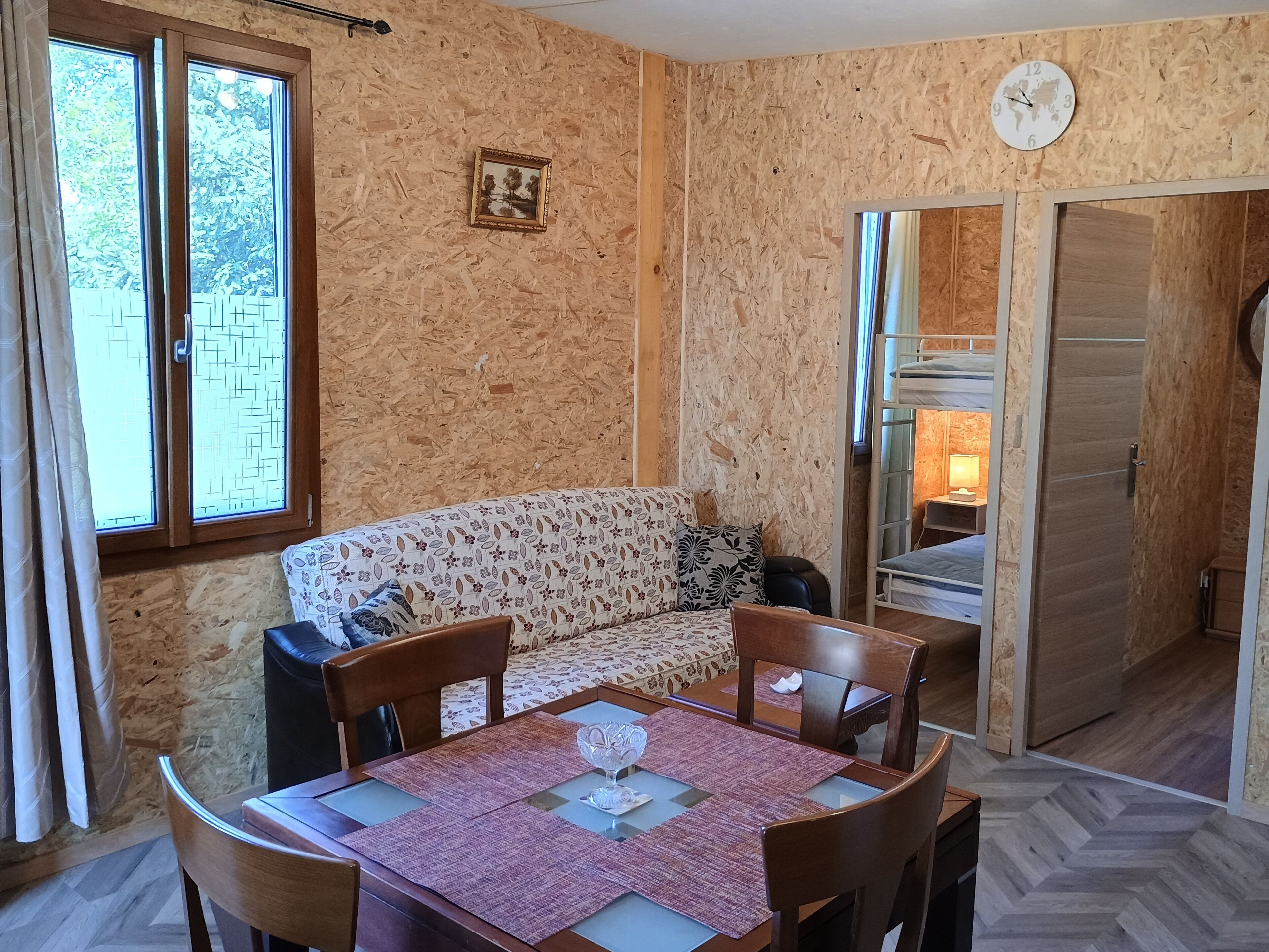Une pièce avec un mur en bois, un canapé, une table à manger avec des chaises, un lit superposé et une horloge.