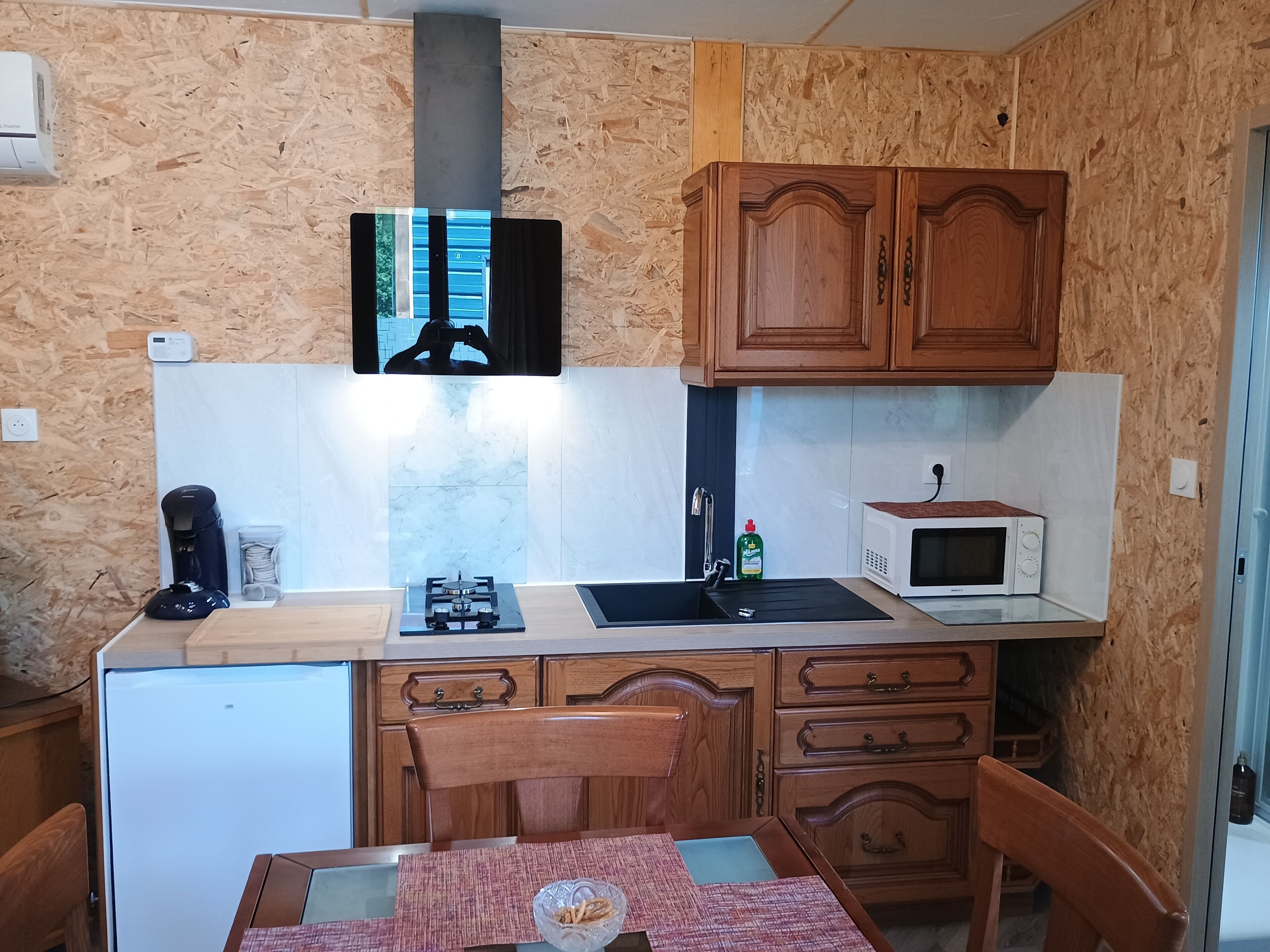 A compact kitchen with wooden cabinets, a microwave, a gas stove, and a small refrigerator.