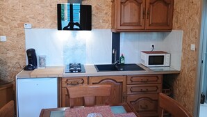 A compact kitchen with wooden cabinets, a microwave, a gas stove, and a small refrigerator.