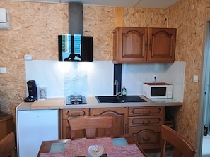 A compact kitchen with wooden cabinets, a microwave, a gas stove, and a small refrigerator.