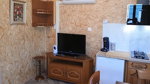 A compact kitchen with a built-in air conditioner, a television on a wooden stand, and a small refrigerator.