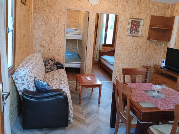 A compact room with a sofa, a small table, a television, and a bunk bed.