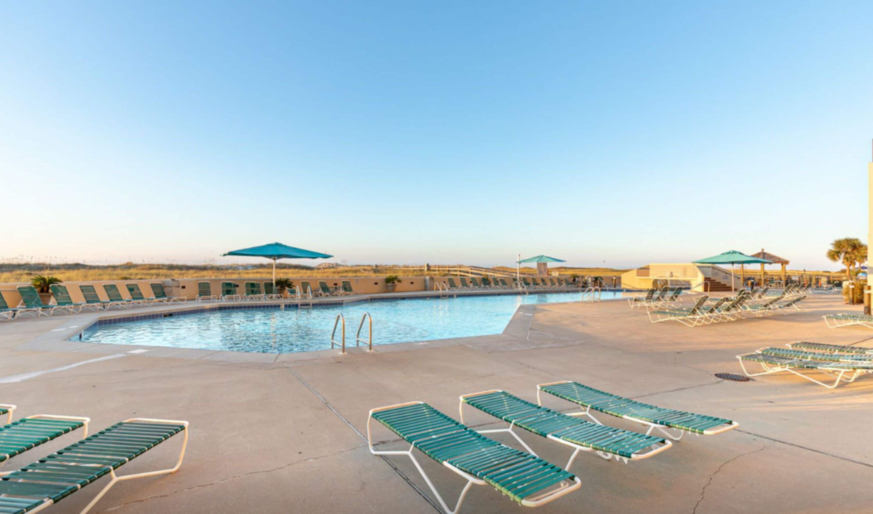 A swimming pool with sun loungers and umbrellas, surrounded by a flat landscape.