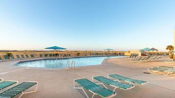 A swimming pool with sun loungers and umbrellas, surrounded by a flat landscape.