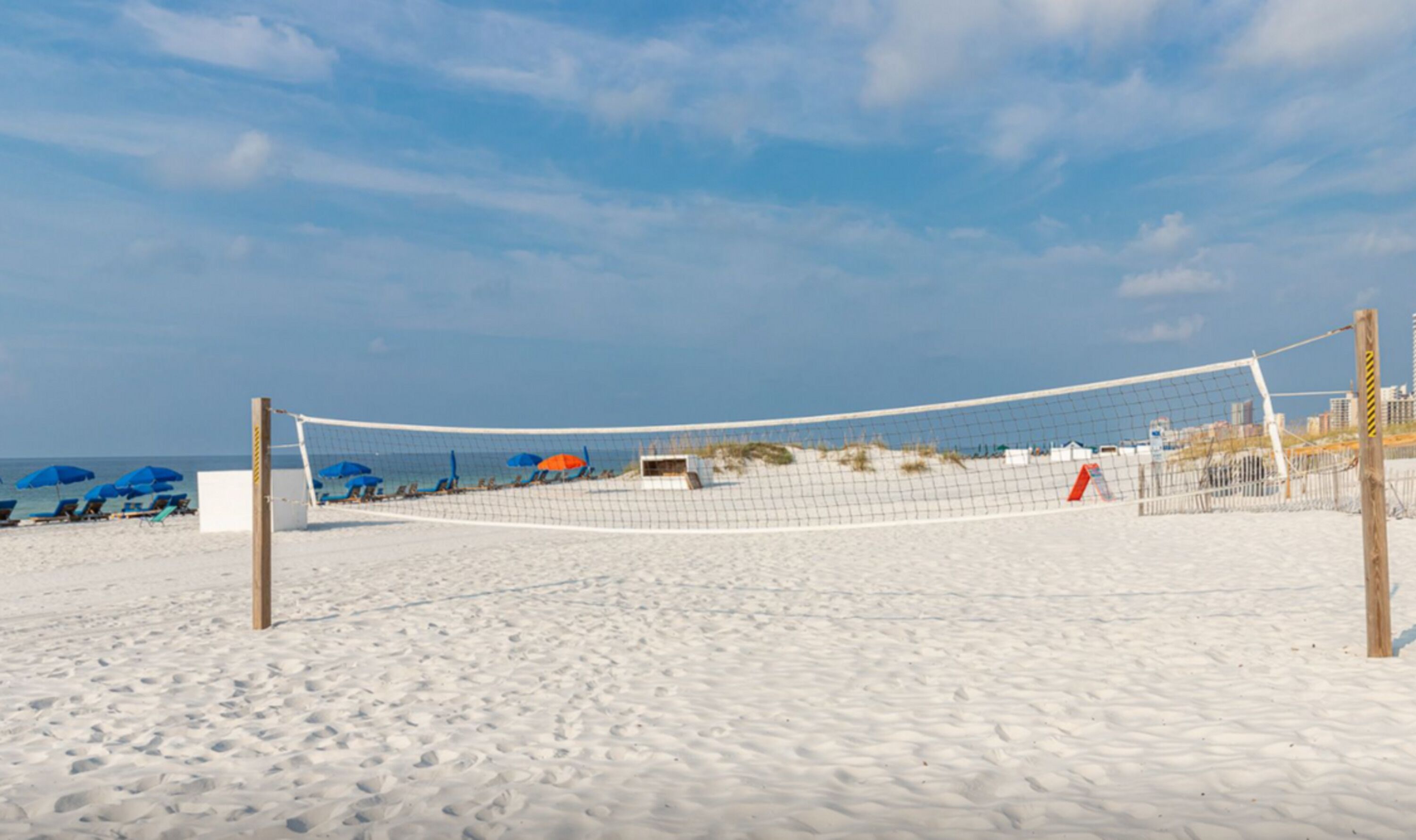 Una red de voleibol de playa sobre arena, con sombrillas y sillas.