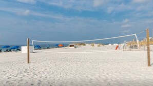 Una red de voleibol de playa sobre arena, con sombrillas y sillas.