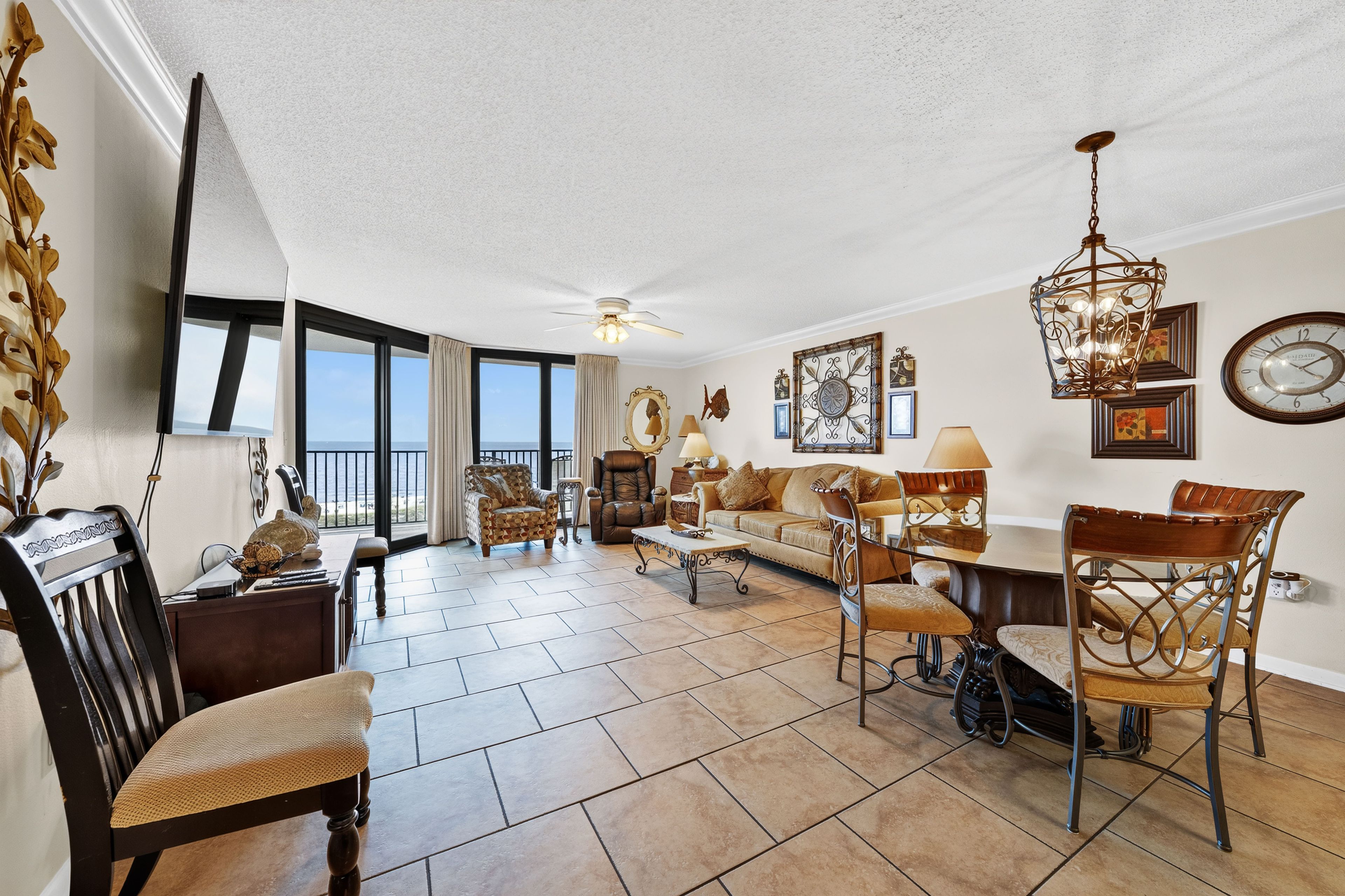 A spacious living room with a large window, a ceiling fan, and a chandelier.