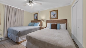 Una habitación de hotel con dos camas individuales, un ventilador de techo, una mesita de noche con lámpara y una puerta.