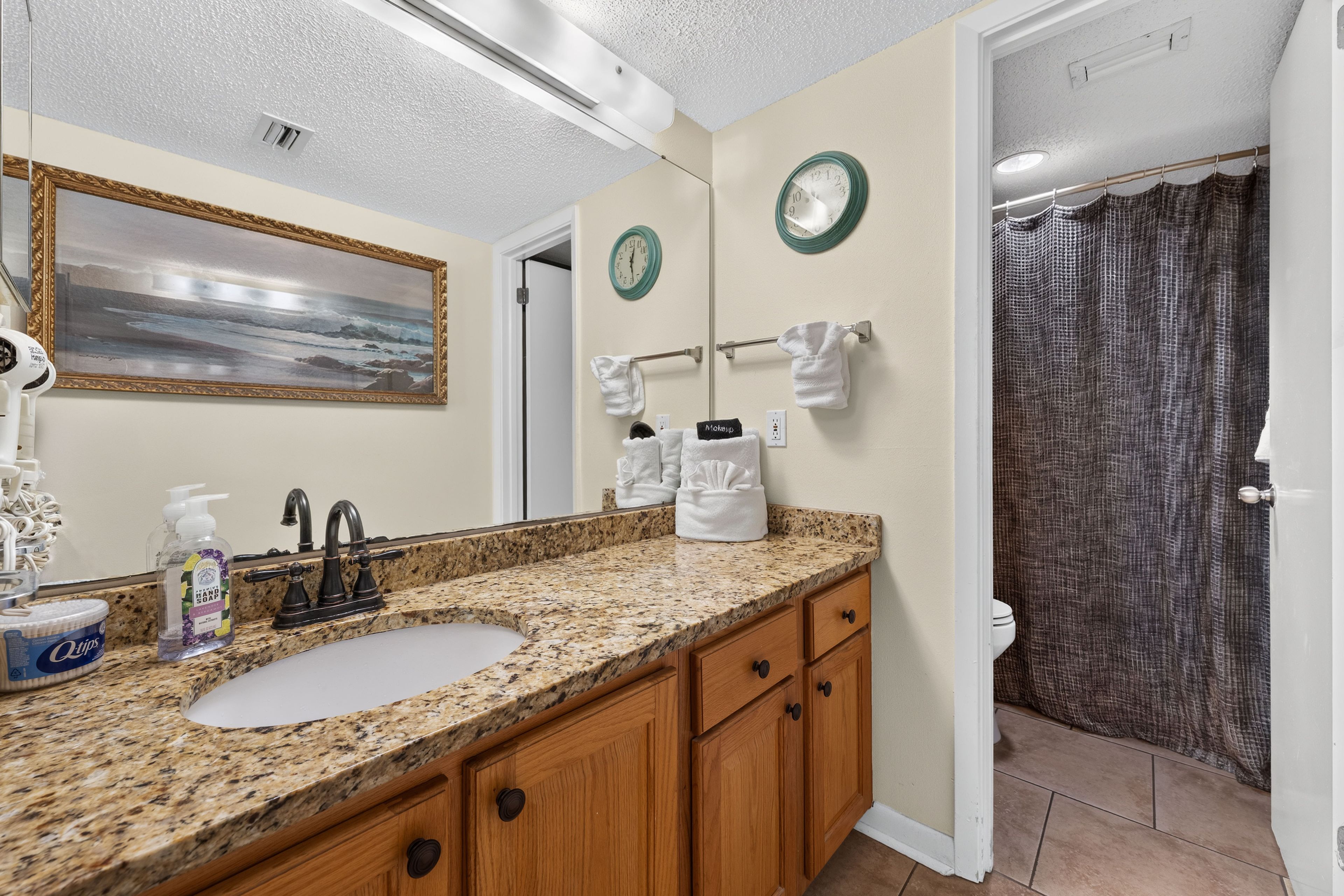 A bathroom with a granite countertop, a sink, a mirror, a towel rack, and a shower curtain.