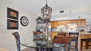 Un comedor con una mesa de vidrio rodeada de sillas, un candelabro y relojes en la pared.