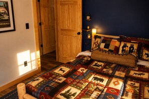 Una habitación con una cama cubierta por un edredón estampado, puertas de madera y una lámpara fijada a la pared.