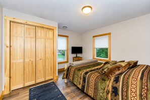 A bedroom with a large wardrobe, a bed with patterned bedding, a television, and a window with a view of greenery. - CHILLBILLY BOLTON-Cozy & Convenient 3BR/2BA ADK home W/HOT TUB in Bolton Landing (Bolton Landing)