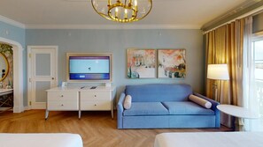 A hotel room with a television, a sofa, a small table, and artwork on the wall. - Orlando | Disney Magic Experience | Pool + Spa (Lake Buena Vista)