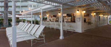A covered outdoor seating area with white chairs and a bar area with a counter and lights.