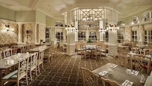 A formal dining area with multiple tables and chairs, a patterned carpet, and decorative wall sconces. - Orlando | Disney Magic Experience | Pool + Spa (Lake Buena Vista)
