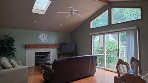 A living room with a fireplace, a television, a ceiling fan, and a view of the outdoors through large windows. - Quiet Ranch Retreat, Close to Everything with Outdoor Bar & Field Views (Boardman)