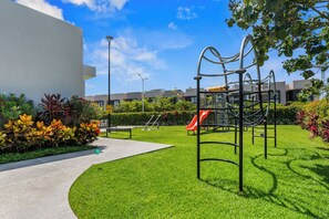 A playground with a slide and climbing structures, surrounded by well-maintained grass and plants. - Casa Ivarica Spacious Home for 16 in Residential (Mezcales)