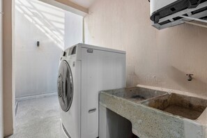 A compact laundry room with a washing machine, a sink, and a small countertop. - Casa Ivarica Spacious Home for 16 in Residential (Mezcales)