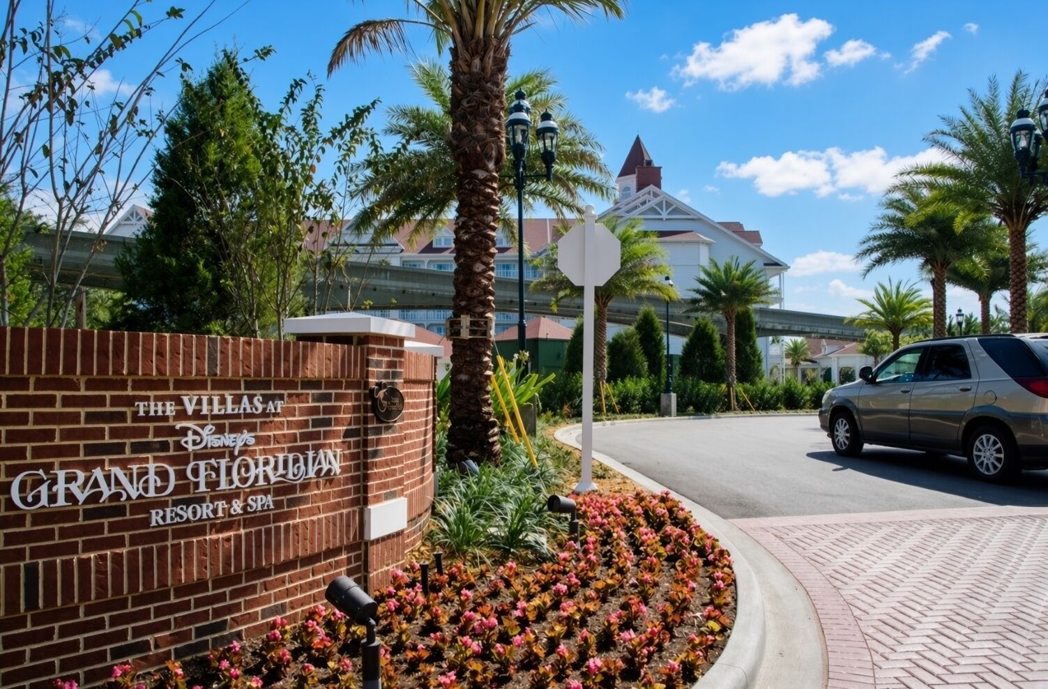 A brick entrance sign for The Villas at Disney's Grand Floridian Resort & Spa, with a palm tree and flower bed in the foreground.