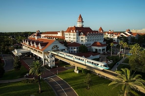 A train station with a modern train, a large white building with a red roof, and palm trees. - Orlando | Elegant Short Stay | Pool + Spa (Lake Buena Vista)