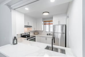 A modern kitchen with white cabinetry, stainless steel appliances, and a marble countertop. - Le Paradis Tranquille: Beautiful Mountain Views! (Mont-Tremblant)