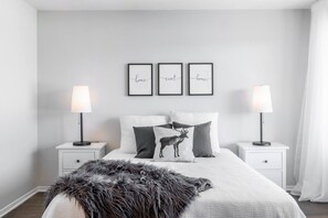 Ein Schlafzimmer mit einem Bett, zwei Nachttischen, einem Fellteppich und drei an der Wand befestigten Bildern.