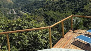 A pool with a view of a valley, wooden deck, and a railing.