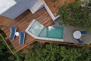 A rooftop pool area with a wooden deck, lounge chairs, and a small table.