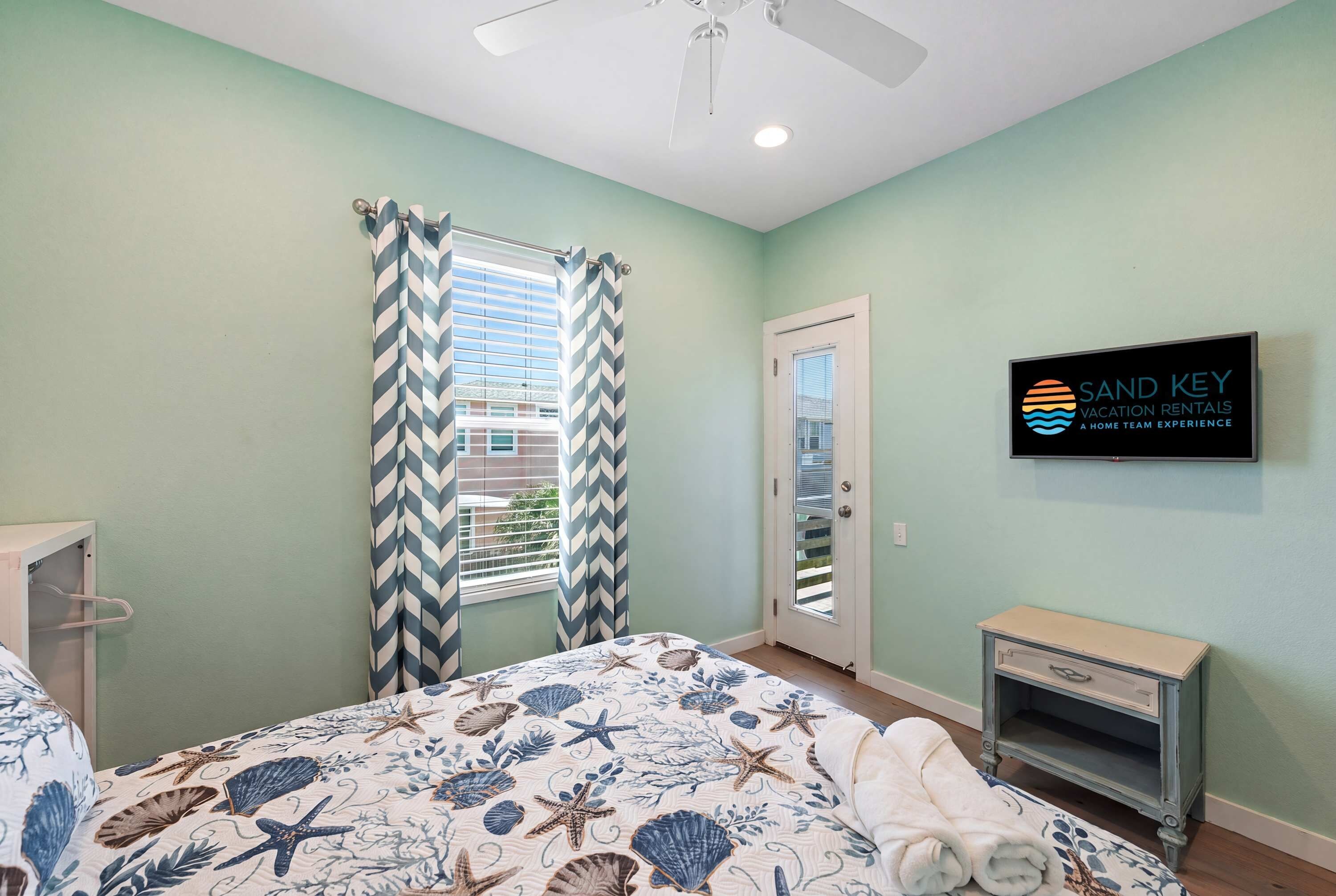 A bedroom with a bed, a nightstand, a TV, and a door with a window.