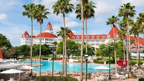 Un resort con una grande piscina, palme e un edificio dai tetti rossi.