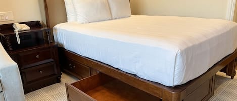 Una habitación de hotel con una cama grande, una mesita de noche con teléfono, un cajón y dos cuadros en la pared.
