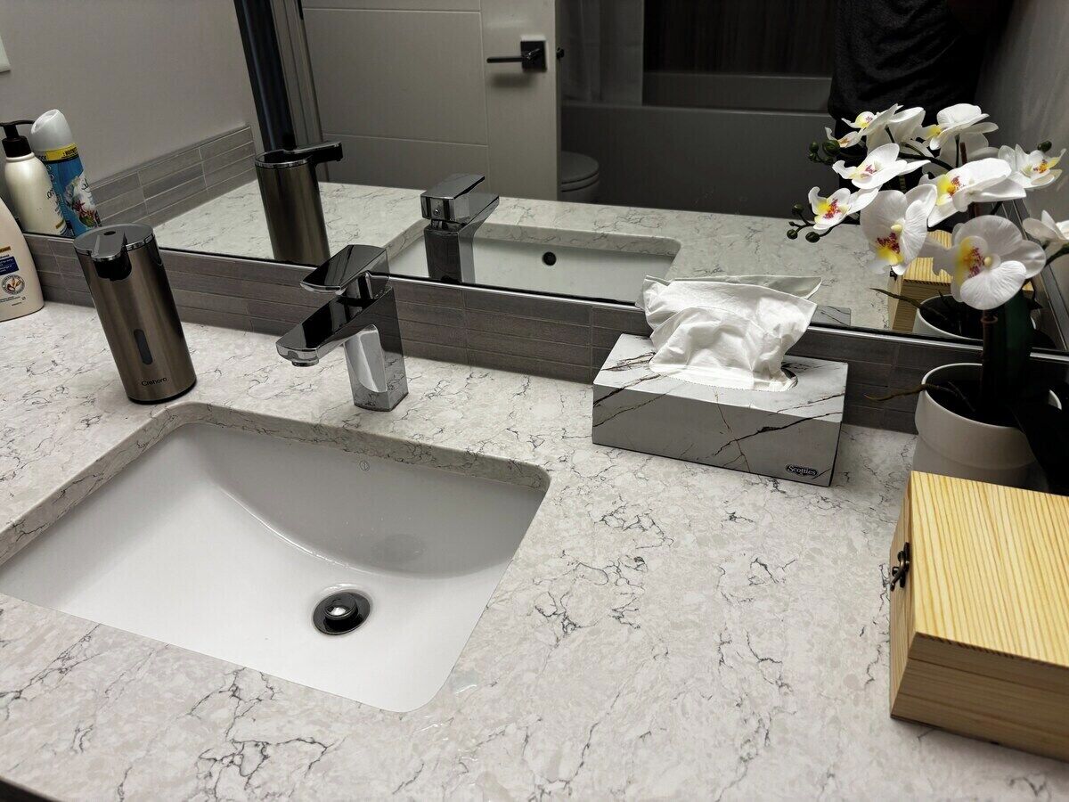 A bathroom with a white sink, a mirror, a towel dispenser, and a vase with white flowers.