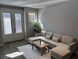 A living room with a sectional sofa, a coffee table, and a white rug. There are two doors with frosted glass windows and a potted plant. - Moose - Private Bedroom near Downtown and 17th Av (Calgary)