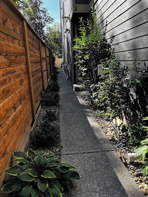 A narrow pathway flanked by wooden fences and vegetation, leading to a building entrance. - Moose - Private Bedroom near Downtown and 17th Av (Calgary)