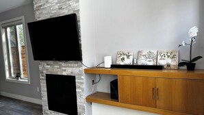 Ein modernes Wohnzimmer mit einem flachbildfernseher über einem Kamin, Holzkästen darunter und Dekorationen auf dem Kaminvorsatz.