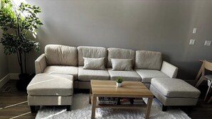 Ein Wohnzimmer mit einem Ecksofa, einem Couchtisch aus Holz und einem weißen Shaggy-Teppich.