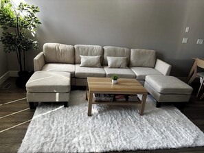 Ein Wohnzimmer mit einem Ecksofa, einem Couchtisch aus Holz und einem weißen Shaggy-Teppich.