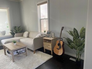 A living room with a sofa, a coffee table, a guitar, a small wooden side table, and a potted plant. - Beaver - Private Bedroom near DT and 17th Av (Calgary)