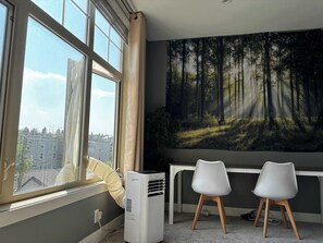 A room with a large window, an air conditioning unit, two white chairs, and a forest-themed wall mural.