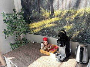 Ein Holztisch mit einer Kaffeemaschine, einem Wasserkocher und einer Kapselbox.