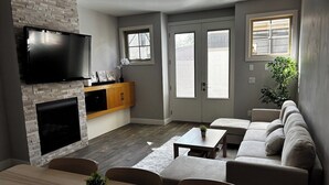 A modern living room with a fireplace, a flat-screen TV, a sofa, and a dining area. - Grizzly - Private Luxury Unit near DT and 17th Av (Calgary)