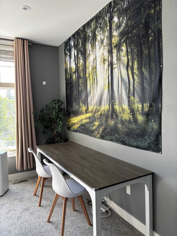 A modern office space with a large forest-themed wall art, a desk, two chairs, and a potted plant.